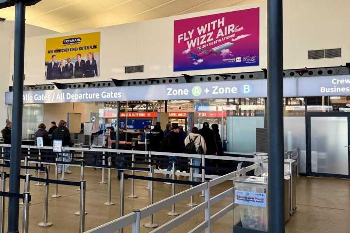 People queueing at airport check-in area under airline advertisements.