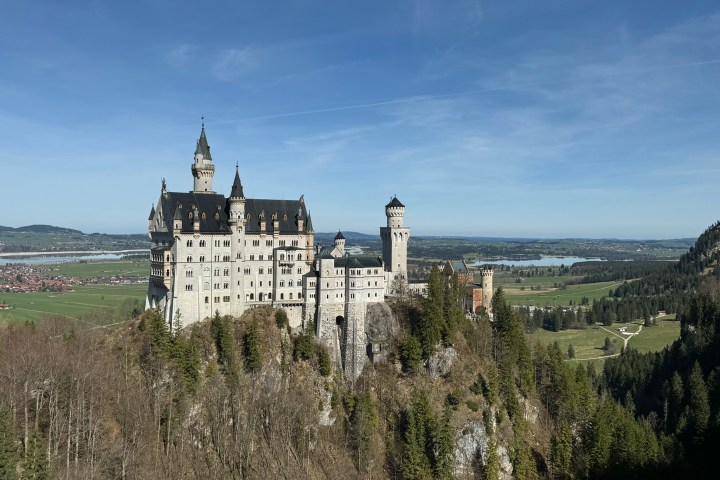 Neuschwanstein Castle on a hill with forest and clear sky.