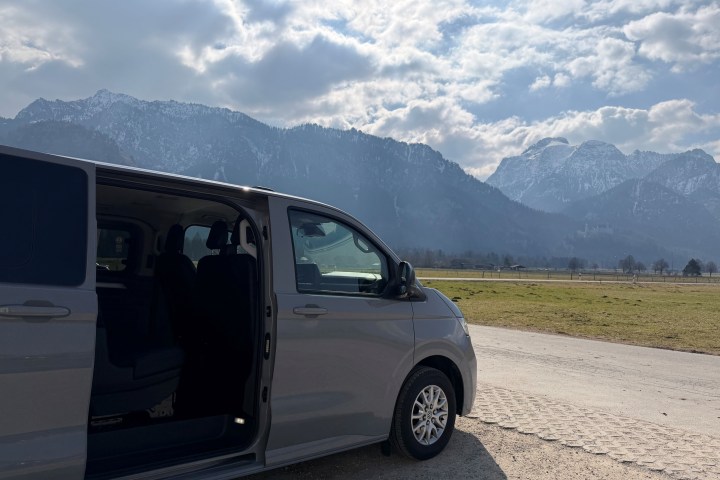 Van with open sliding door parked on mountain road under cloudy sky.