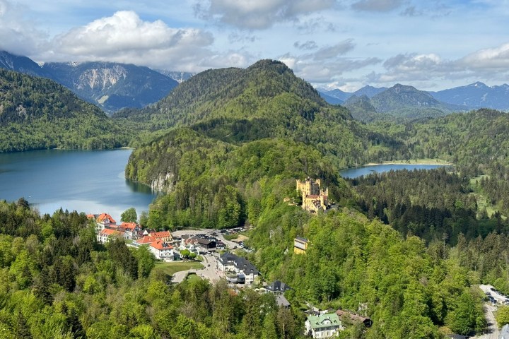 Scenic view of Hohenschwangau Castle with lake, hills, and forests.