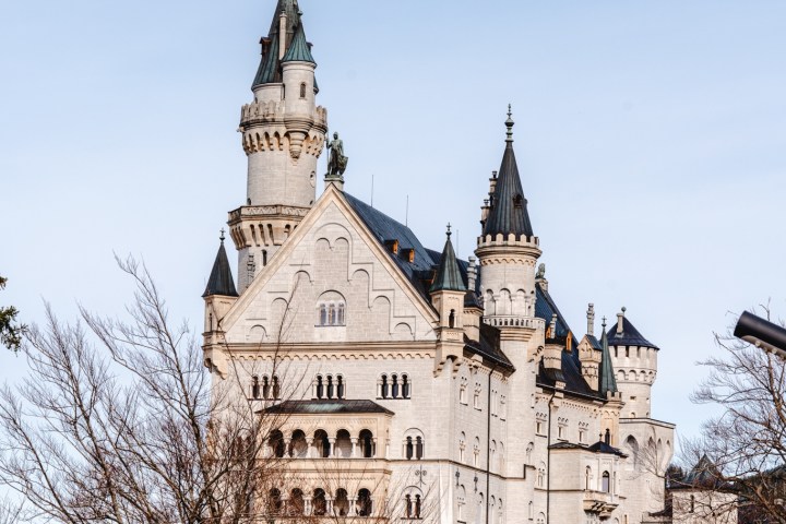 White fairytale castle with turrets behind leafless trees under a clear blue sky.