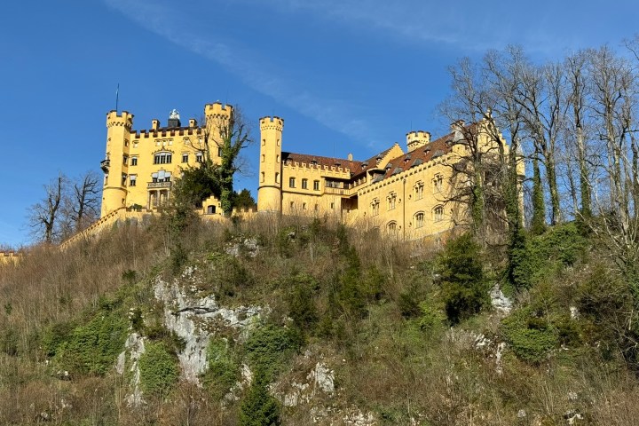 A yellow castle with towers on a hill under a clear blue sky.