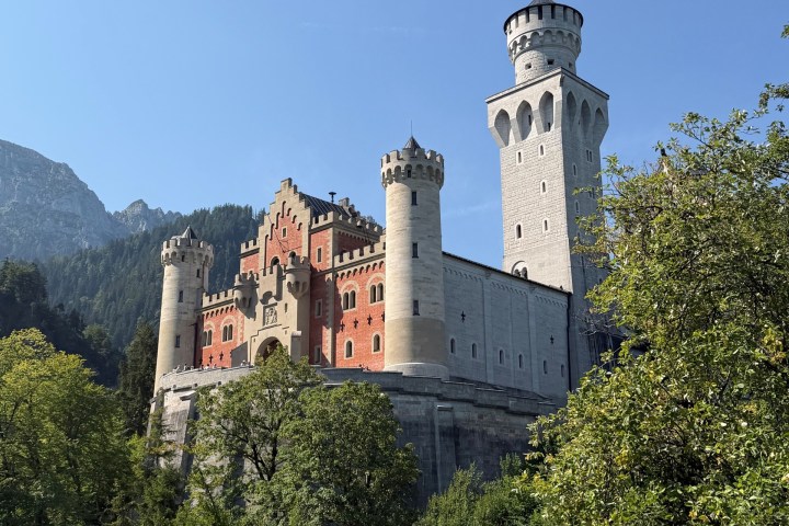 Neuschwanstein Castle with trees and mountains in the background on a clear day.