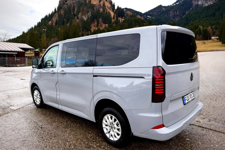 Gray van parked on wet road with mountains in background.